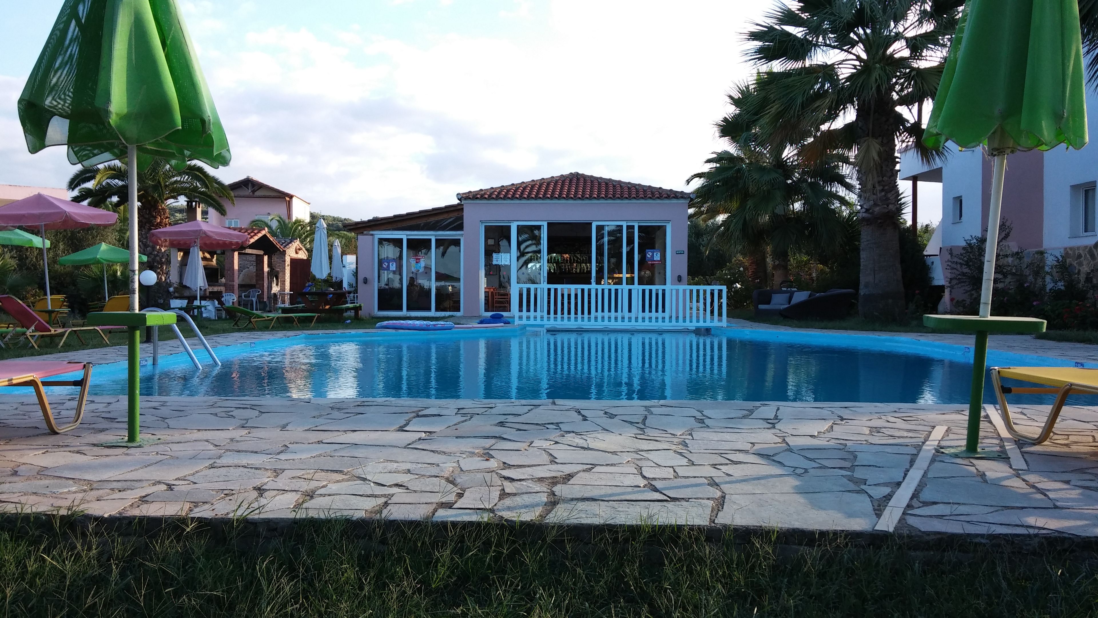 Una piscina con sillas de descanso y sombrillas, rodeada de palmeras y edificios.