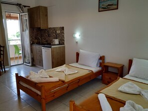 A room with a bed, a small bedside table, a kitchenette, and a sliding door leading to an outdoor area. - Pardalakis Studios (Platanias)