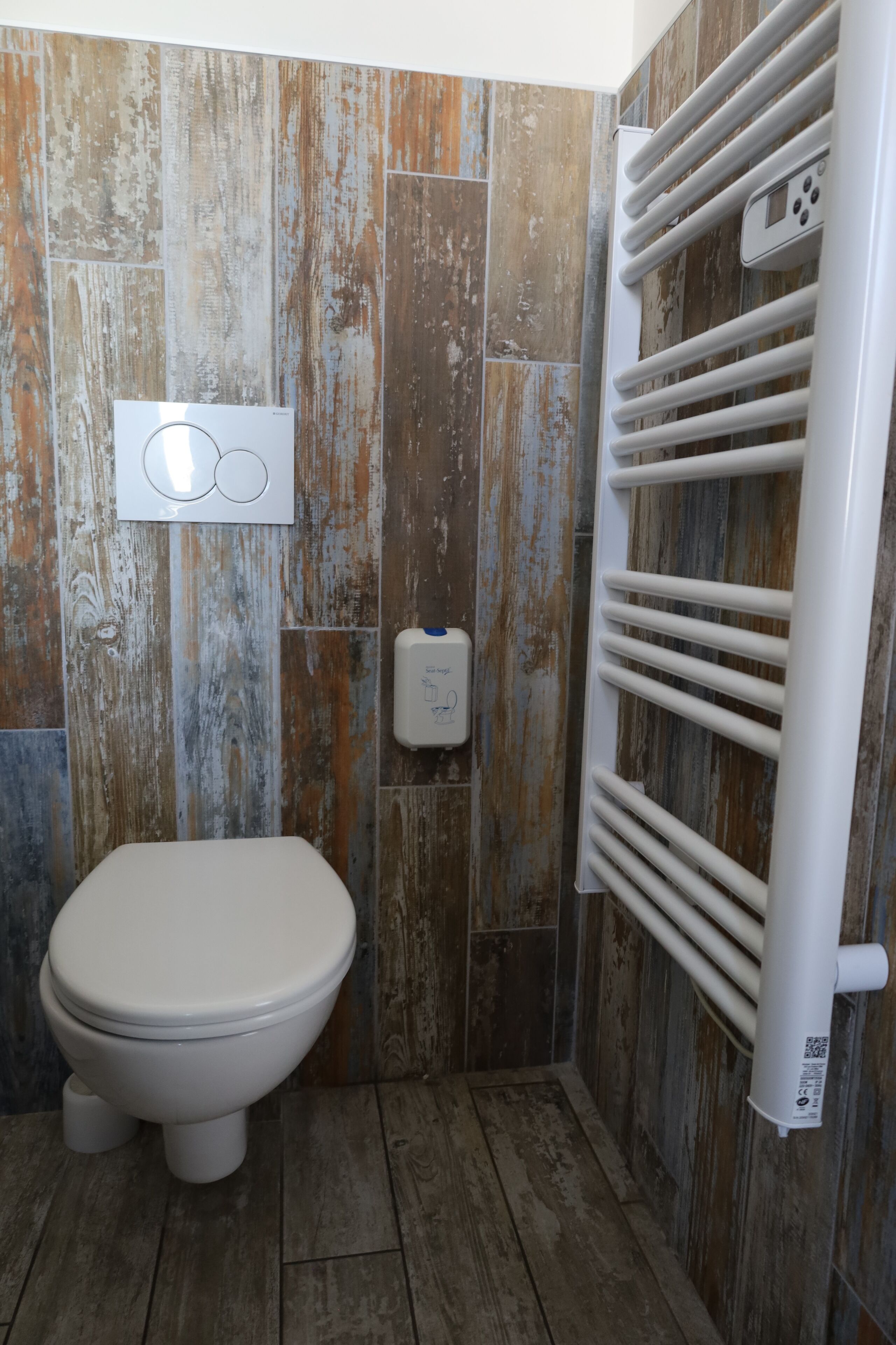 A bathroom with a rustic wooden wall design, a toilet, and a white radiator.