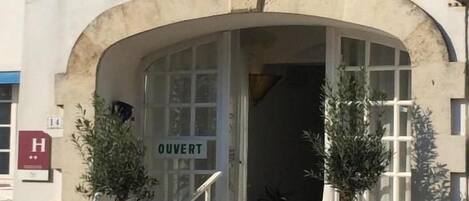 Un hotel llamado 'NEPTUNE' con una entrada en arco, un cartel que indica 'OUVERT' (abierto) y una escalera que lleva a la entrada.