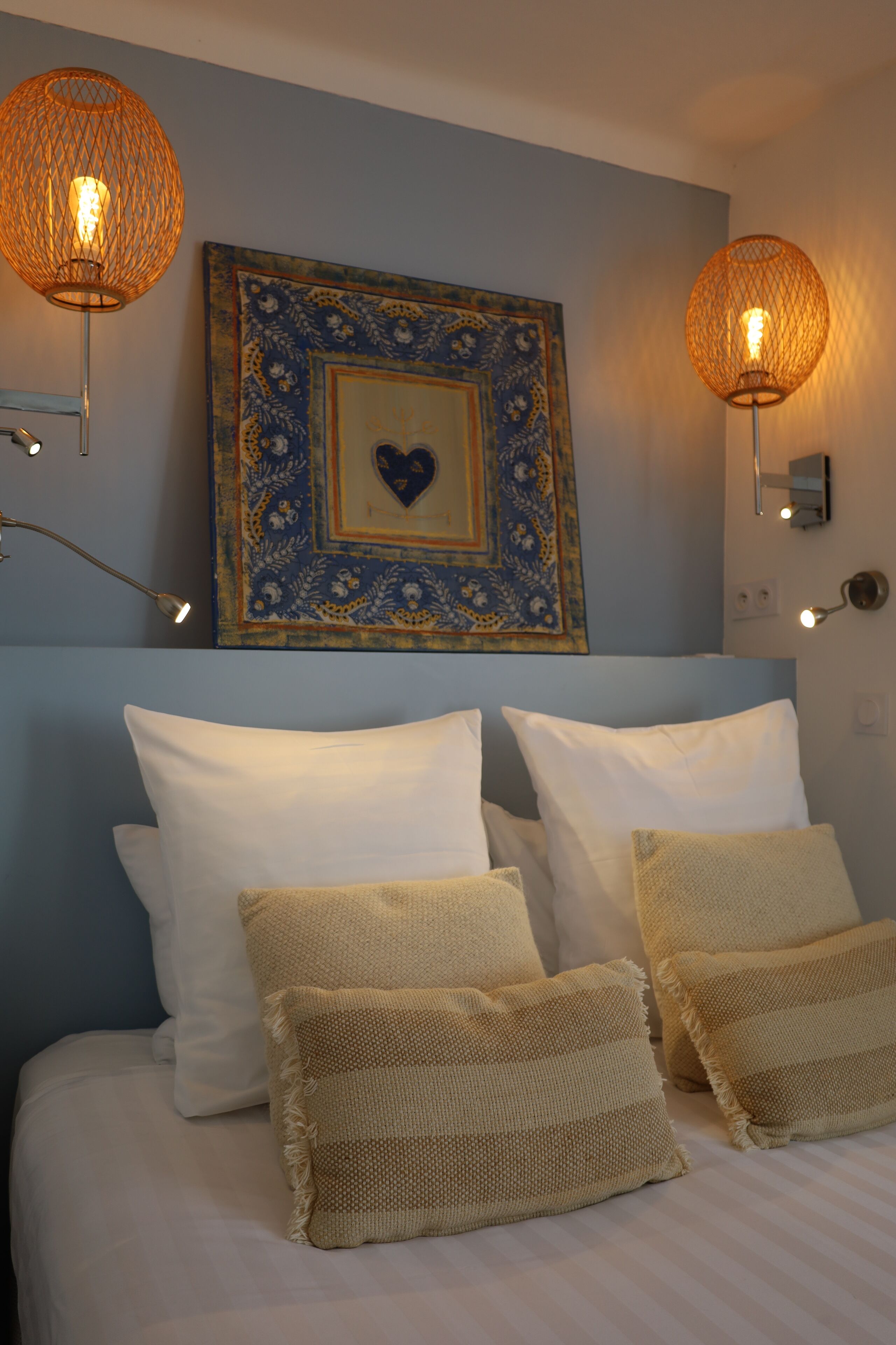 A neatly made bed with white and beige pillows, a decorative wall piece, and two wall-mounted lamps.
