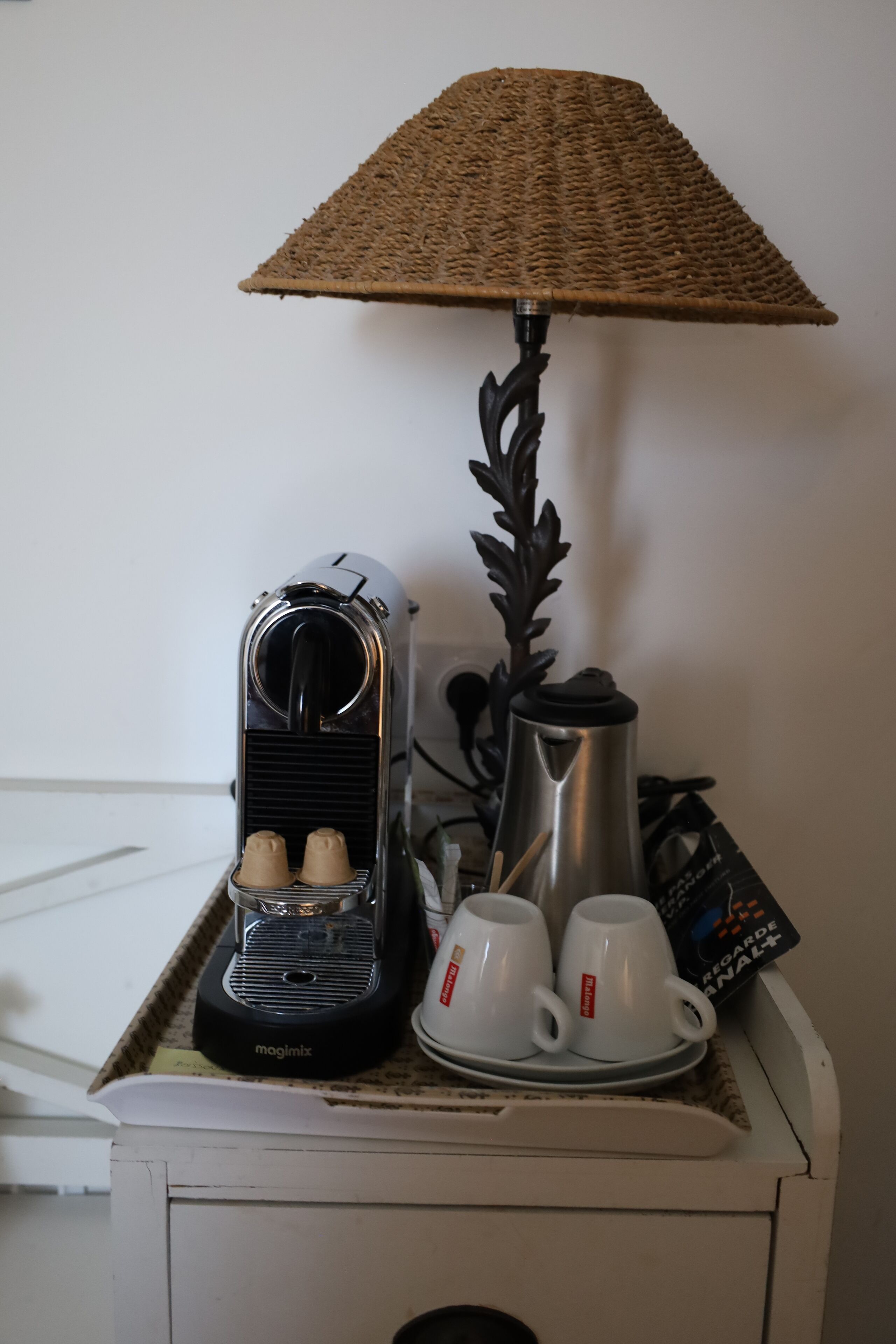 A coffee maker, two cups, a kettle, and a lamp on a table.