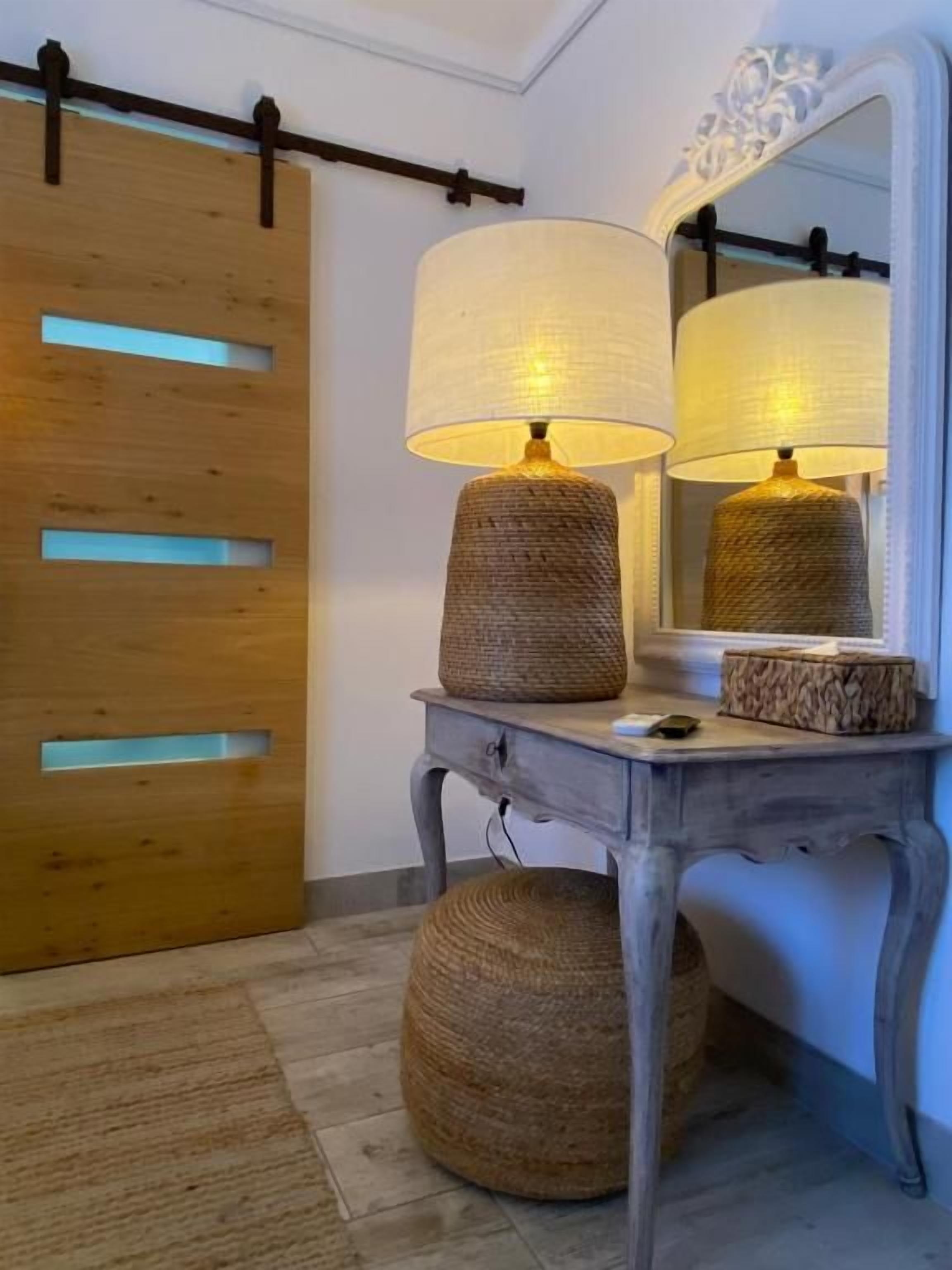 A wooden sliding door with a modern design, a small table with a lamp, and a mirror on the wall.