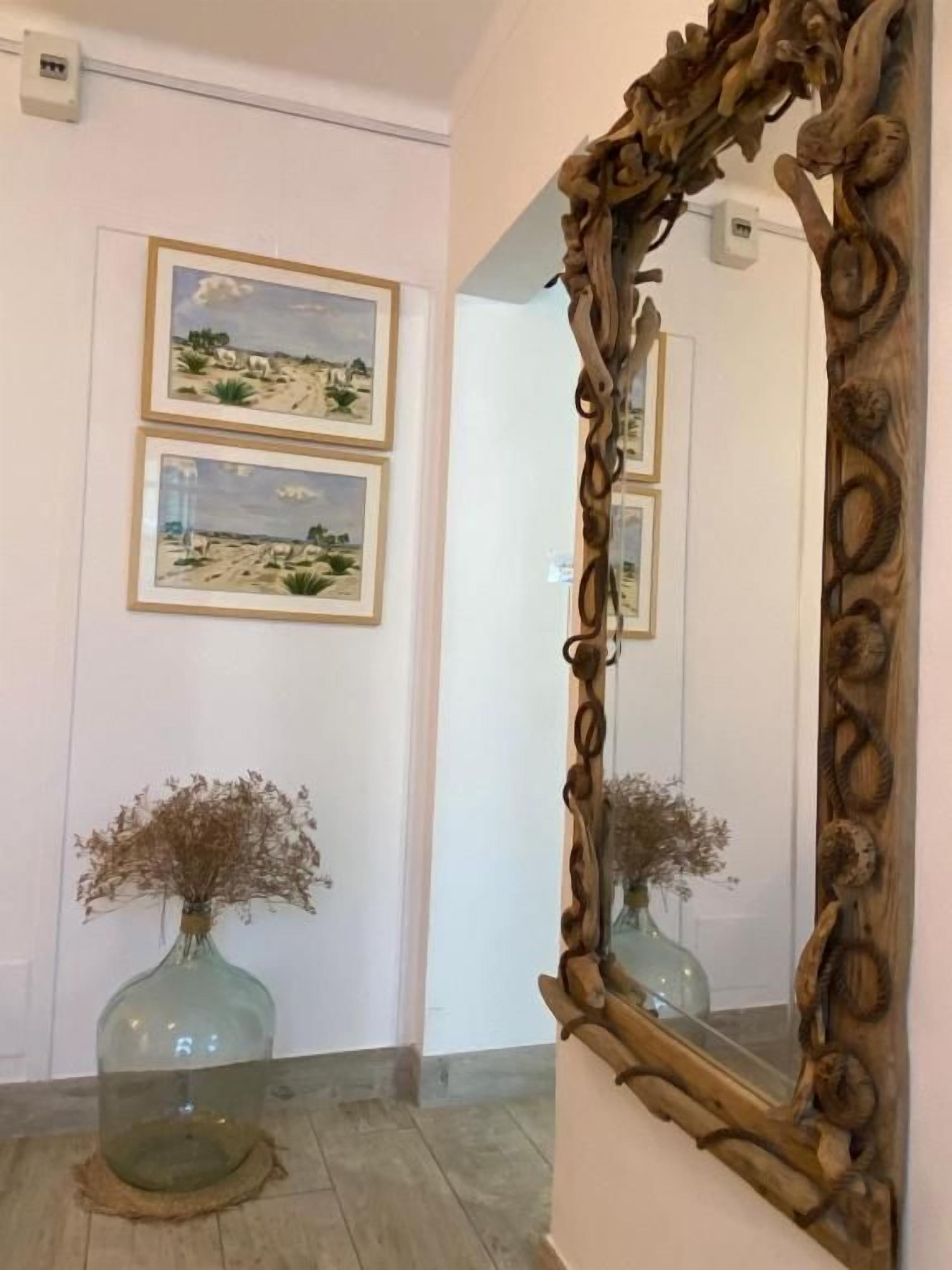 A room with a large mirror, framed by a wooden design, and two framed pictures on the wall.