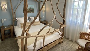 Une chambre à coucher avec un lit à baldaquin fait de branches d’arbres naturelles, une table de chevet en bois, une chaise en osier et un tableau accroché au mur.