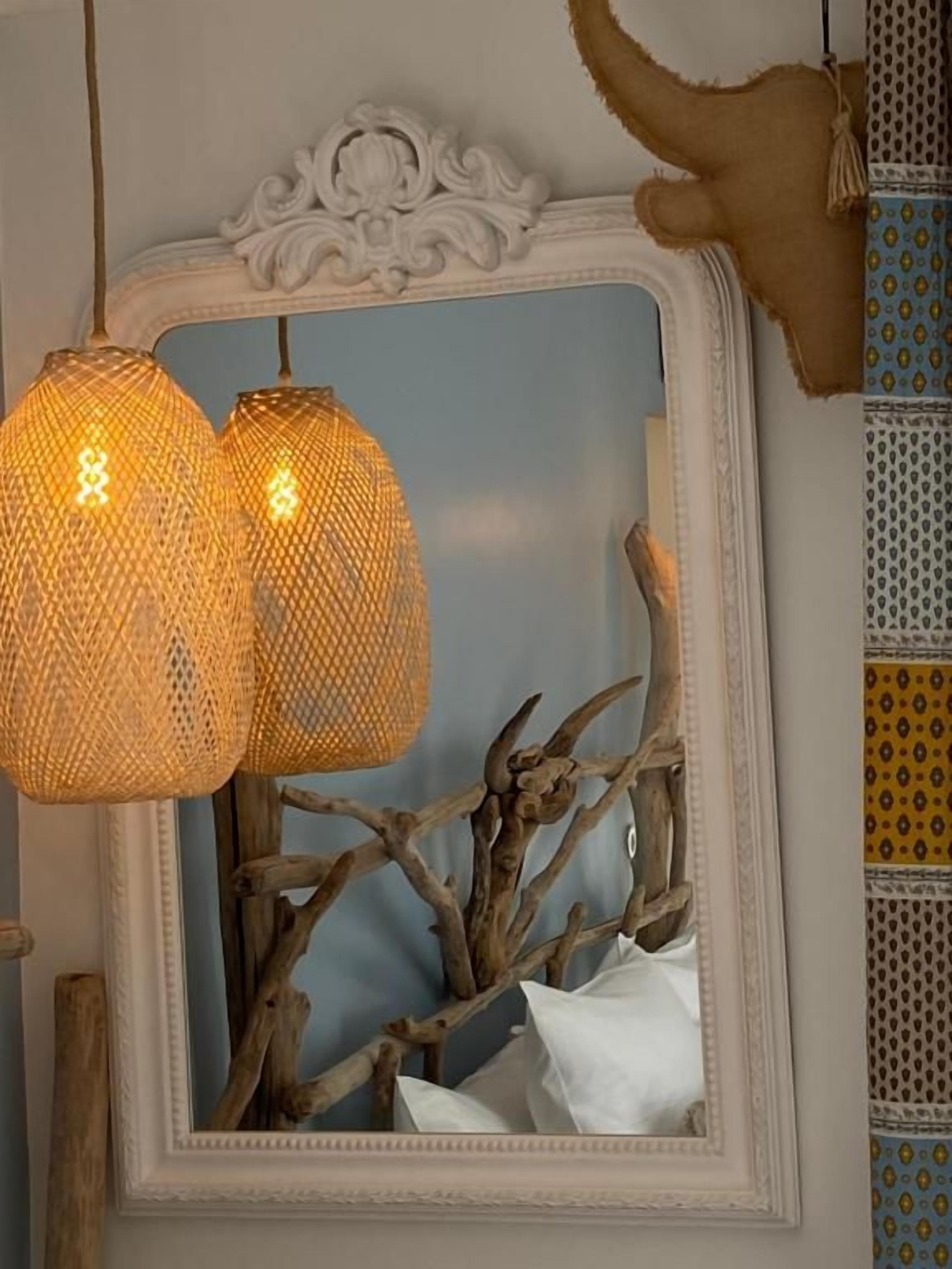 En spegel med en dekorativ ram, två hänglampor med ett vävt mönster och en gren med ett vitt tygstycke.