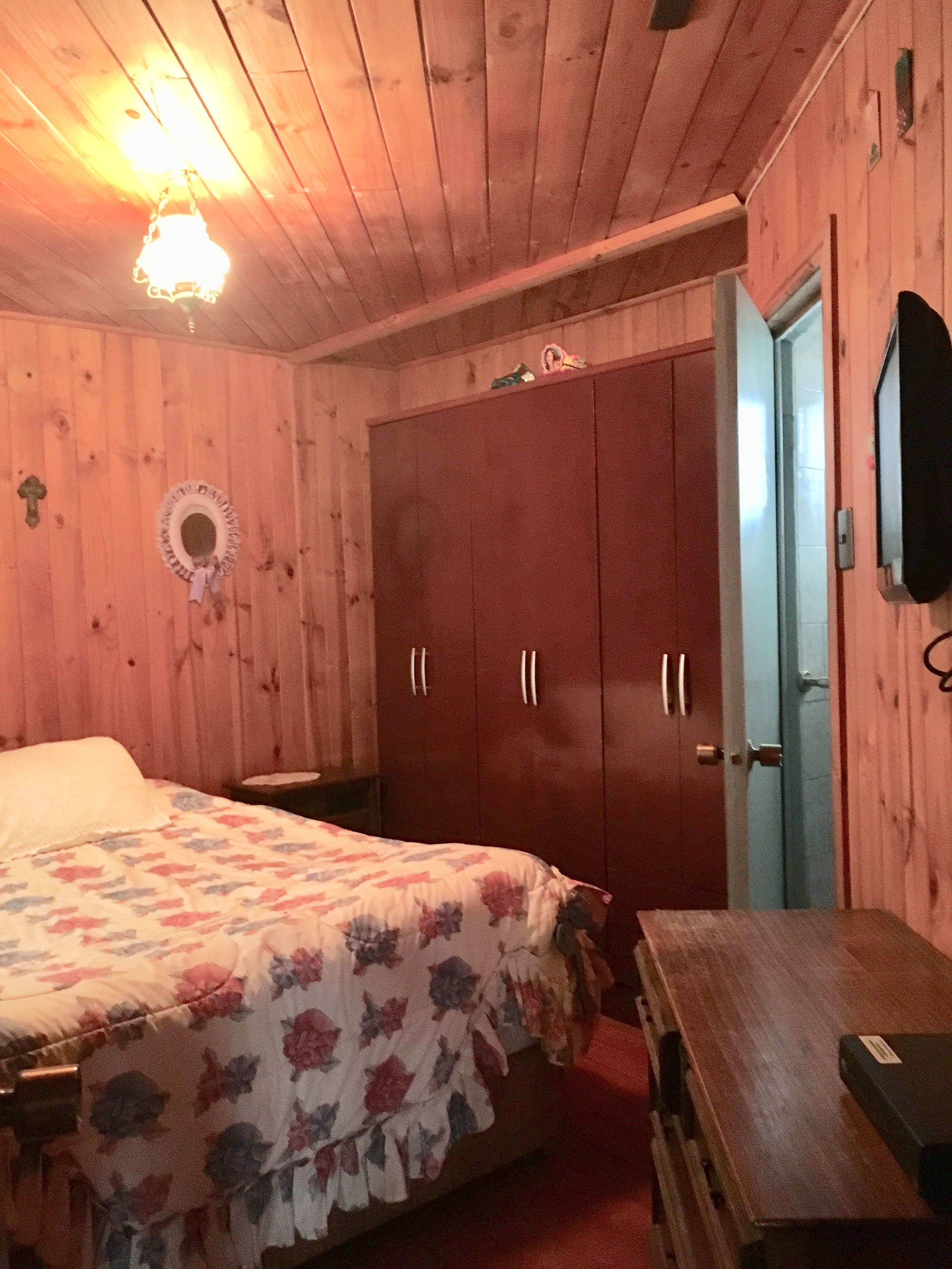 Ein Zimmer mit Holzboden, einem Bett, einem Kleiderschrank, einem Schreibtisch und einem Fernseher.