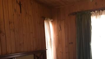 Quarto de madeira com cama, mesa de cabeceira, cruz na parede e lustre.