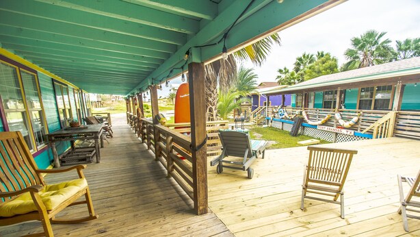 A wooden deck with rocking chairs and tables, a covered area with a green roof, and a sign reading "Port Aransas, TX".