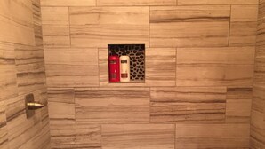 A shower with a tiled wall and a pebble-patterned floor.