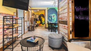A cozy interior with a flat-screen TV, a chalkboard sign reading "Welcome to The Rock & Roll Hall of Fame", and a bookshelf with books and magazines.