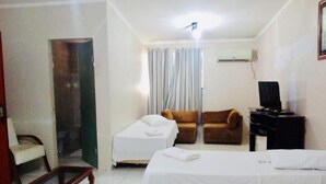 A hotel room with a bed, two chairs, a small table, a TV, and a window with curtains. - Hotel Castelo (Palmas)