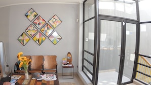 A room with a wooden sofa, a dining table with a vase of sunflowers, and a wall with geometric wall art. - Loft Cielo Abierto (Valparaiso)