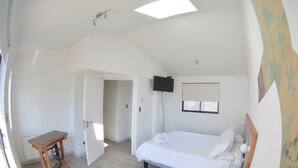 A bedroom with a bed, a small table, a TV mounted on the wall, and a window. - Loft Cielo Abierto (Valparaiso)