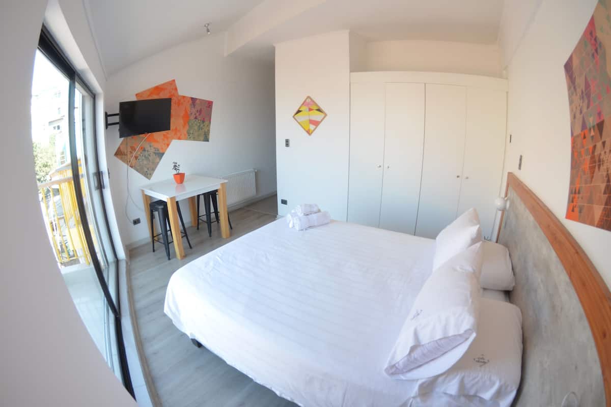 Une chambre avec un grand lit, un bureau, une chaise et un téléviseur fixé au mur.