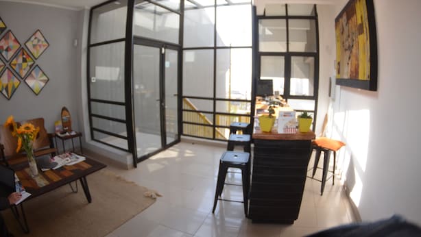 A modern living room with a glass door leading to a balcony, a wooden coffee table, a sofa, and a small kitchen area with stools. - Loft Cielo Abierto (Valparaiso)