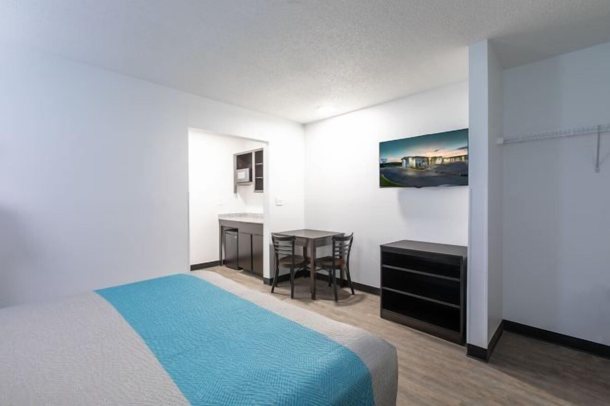 A compact hotel room with a bed, a small desk, a chair, and a wall-mounted TV.
