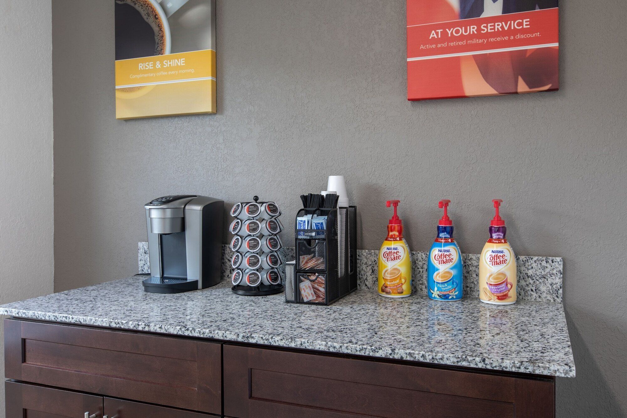 A coffee station with a coffee maker, a coffee grinder, a coffee pod holder, and three bottles of Nespresso coffee creamer.