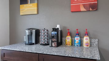 A coffee station with a coffee maker, a coffee grinder, a coffee pod holder, and three bottles of Nespresso coffee creamer.