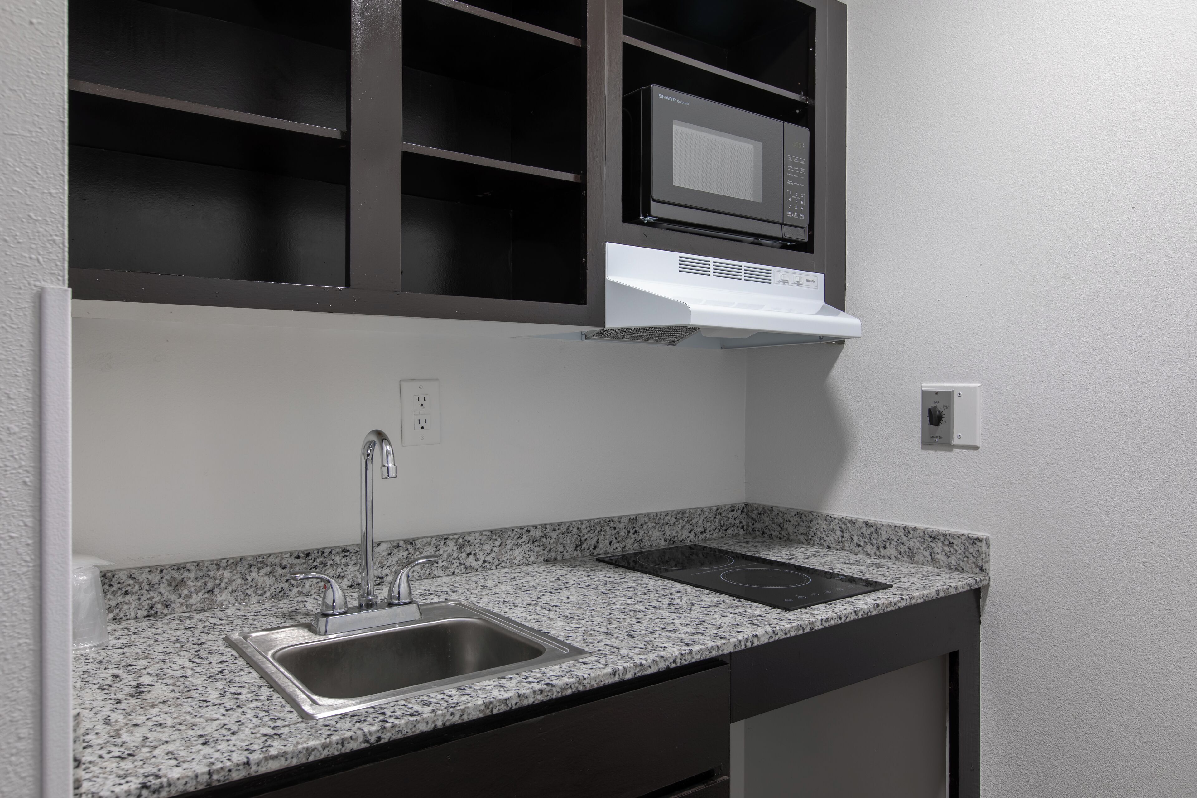A kitchen with a granite countertop, stainless steel sink, black cabinets, a microwave, and an induction cooktop.