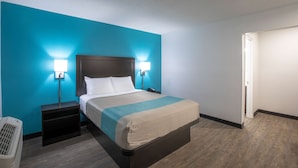 A hotel room with a bed, two bedside tables, a nightstand, and a wall-mounted lamp. - Motel 6 Greenville, SC - I-85 Near Downtown (Greenville)