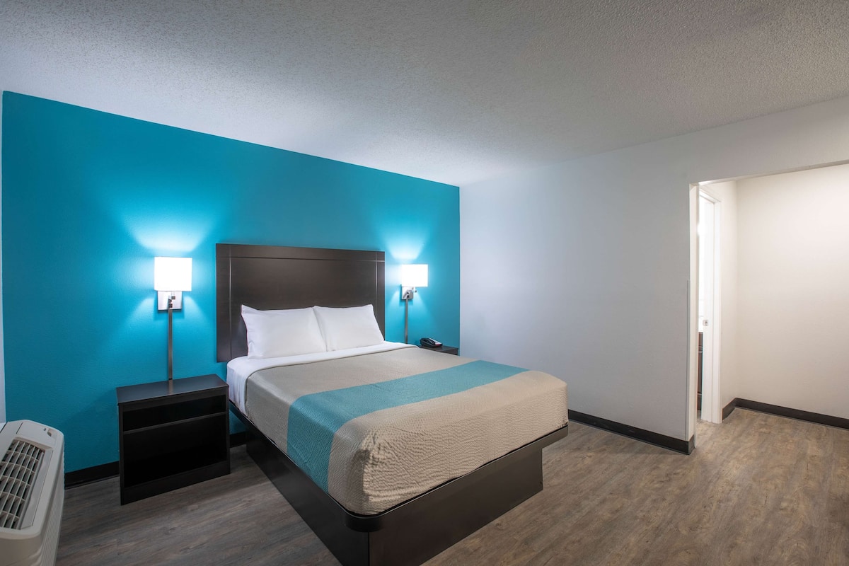 Une chambre d’hôtel comprenant un lit, deux tables de chevet, une petite table et une lampe fixée au mur.