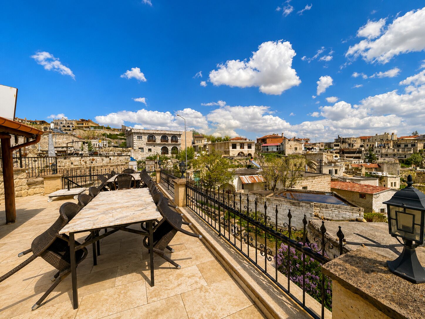 A terrace with a table and chairs, a stone wall, and a view of a hillside town with buildings.