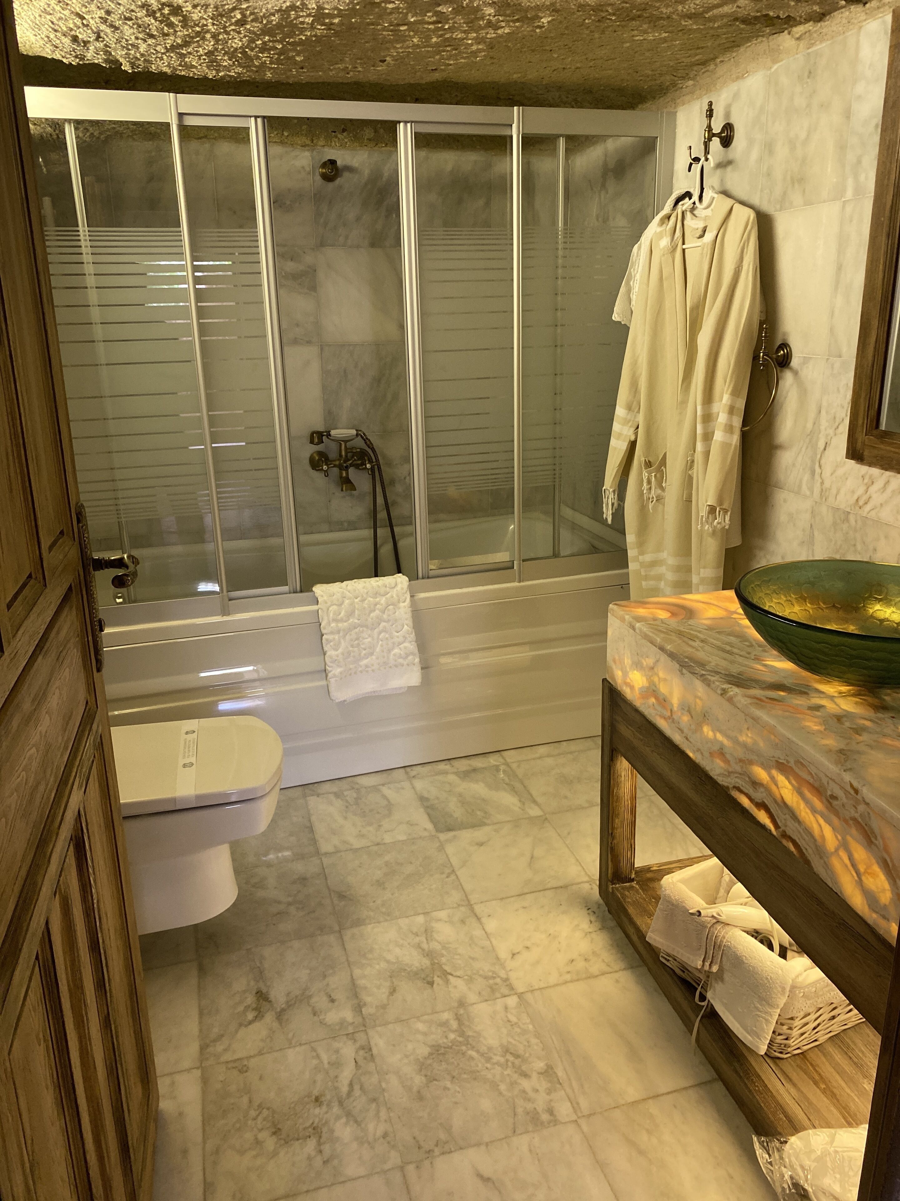 Baño con ducha de vidrio, inodoro blanco y encimera de mármol con lavabo.
