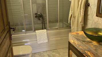 Baño con ducha de vidrio, inodoro blanco y encimera de mármol con lavabo.