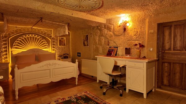 A room with a bed, desk, chair, and a large arched window. - Iris Cave Cappadocia (Ürgüp)
