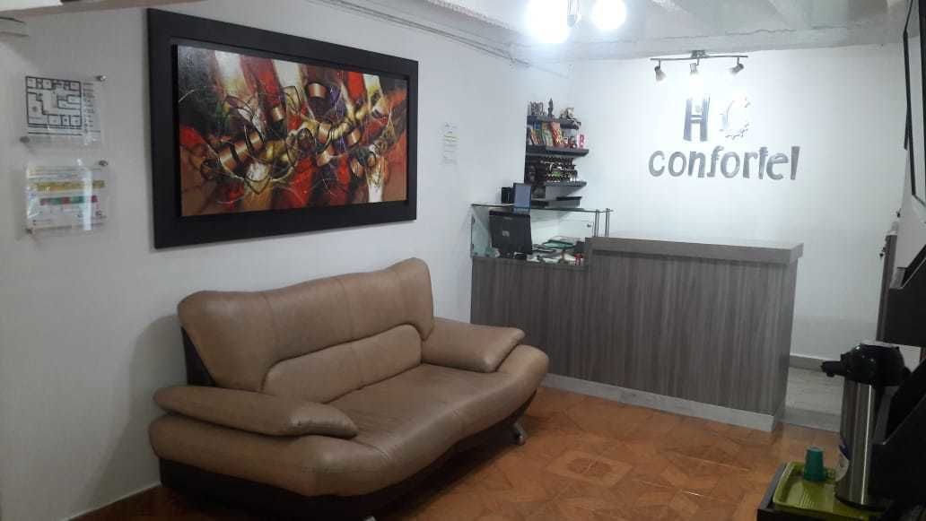 A room with a brown sofa, a framed abstract painting, a reception desk, and a sign that reads "H confortel".
