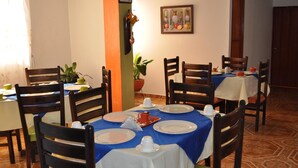 Un comedor con mesas dispuestas para cuatro, sillas, una planta en maceta y un cuadro en la pared.