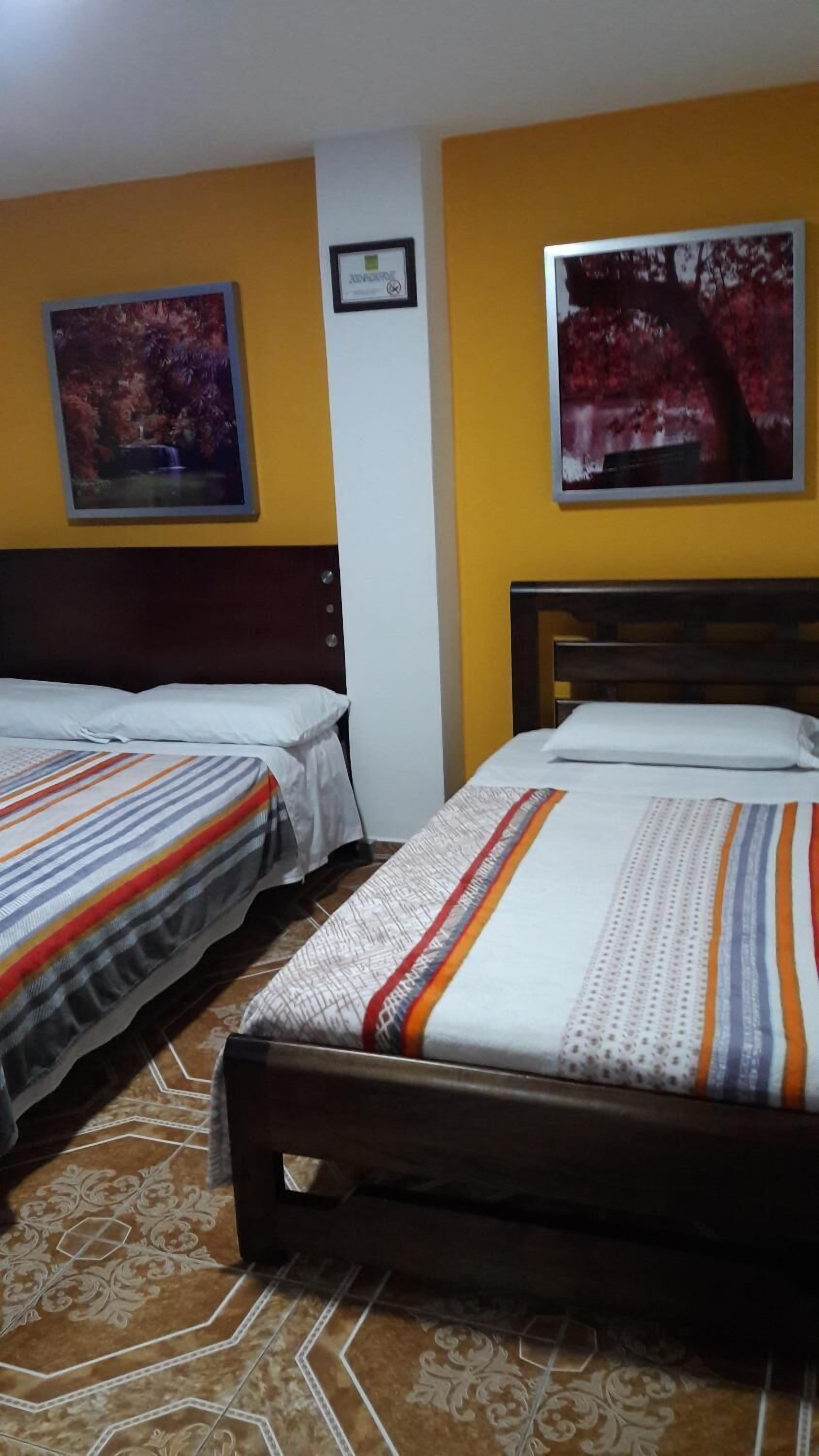 Una habitación de hotel con dos camas individuales, un cabecero de madera y dos cuadros en las paredes.