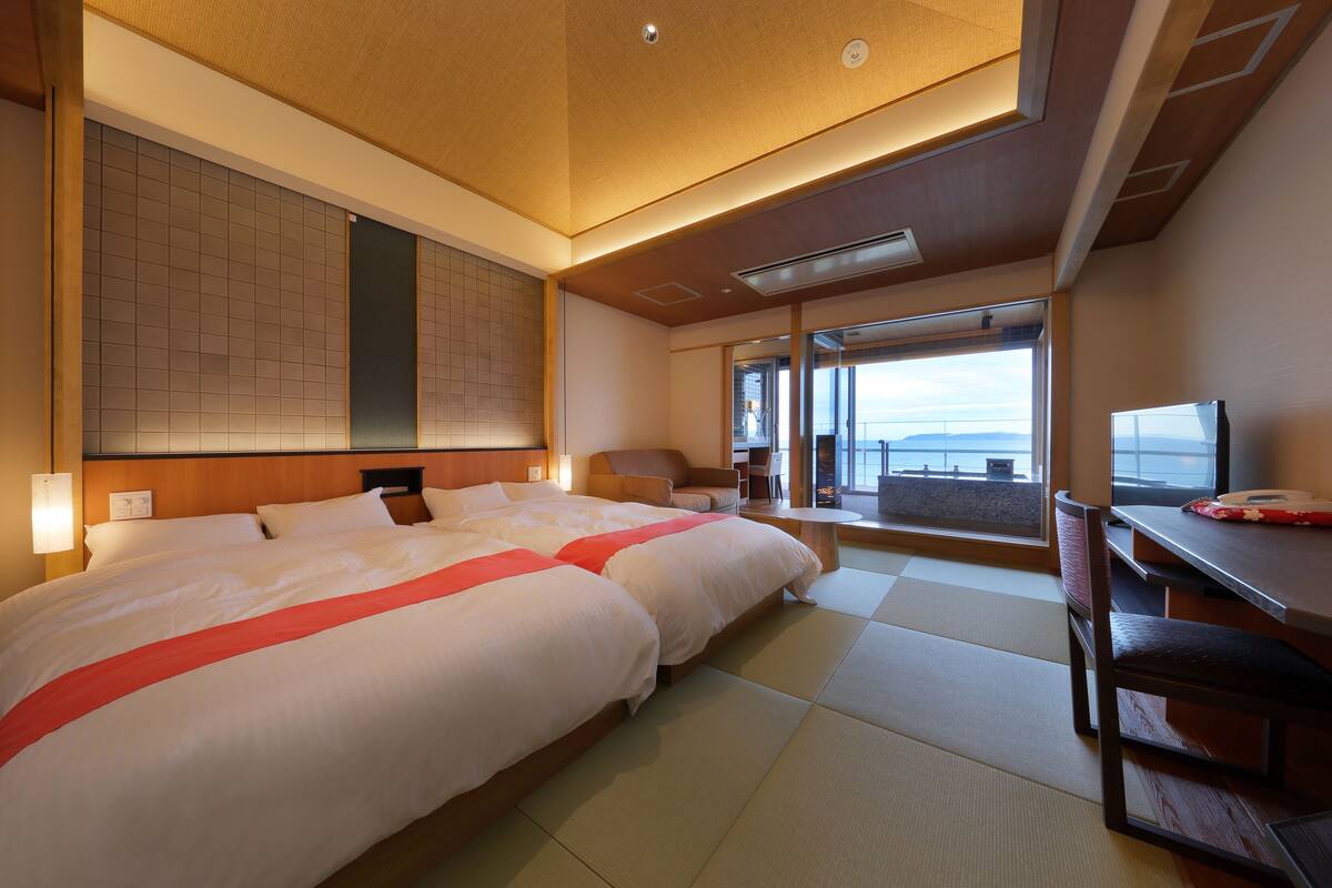A hotel room with a large bed, a desk, and a view of the sea.