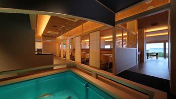 A modern hotel interior with a swimming pool, multiple dining areas, and a view of the outdoors.