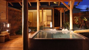Un onsen japonés tradicional con una terraza de madera, una fuente termal de piedra y una estructura de madera en el techo.
