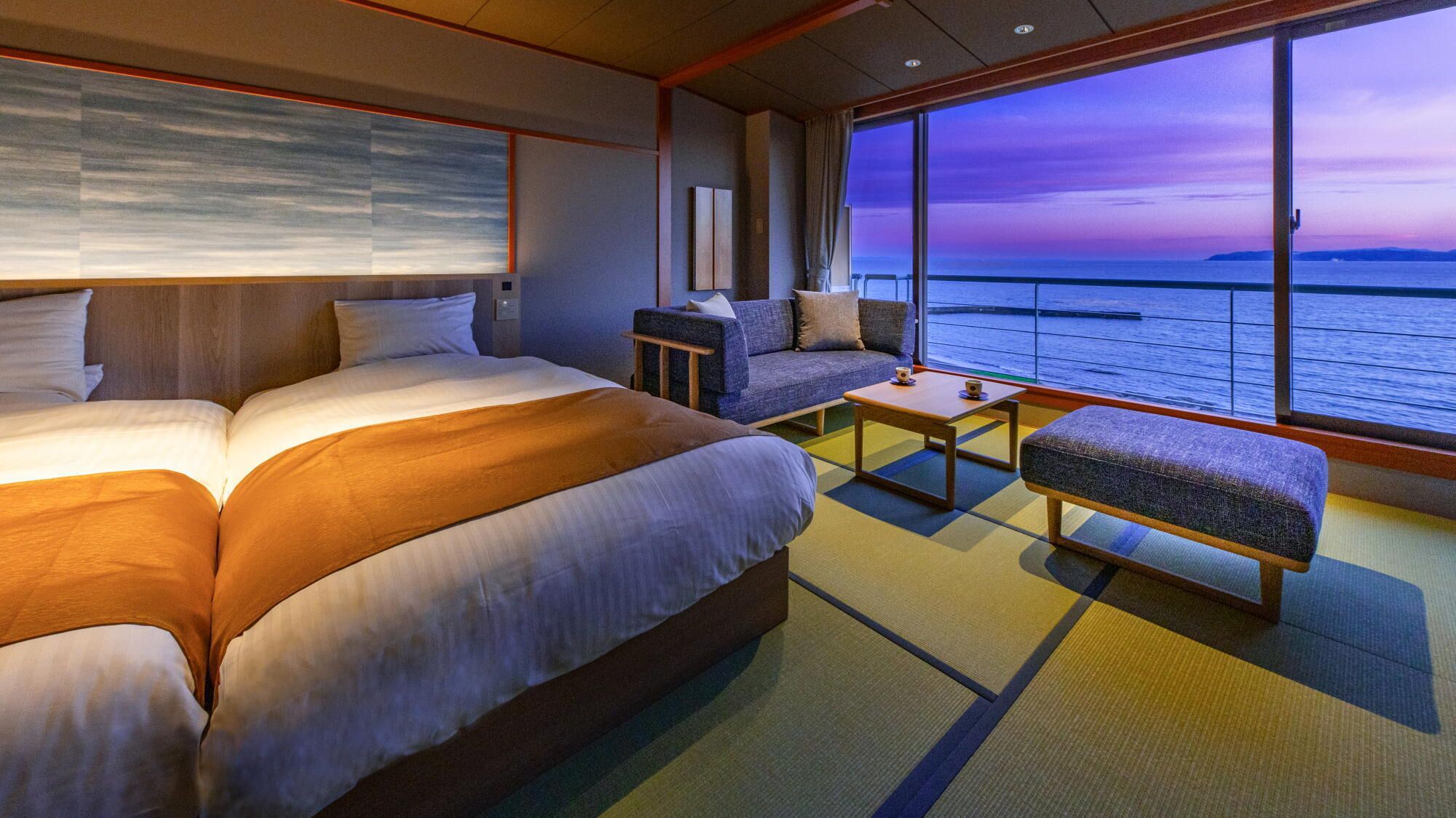 A hotel room with a large bed, a sofa, a small table, and a view of the sea.