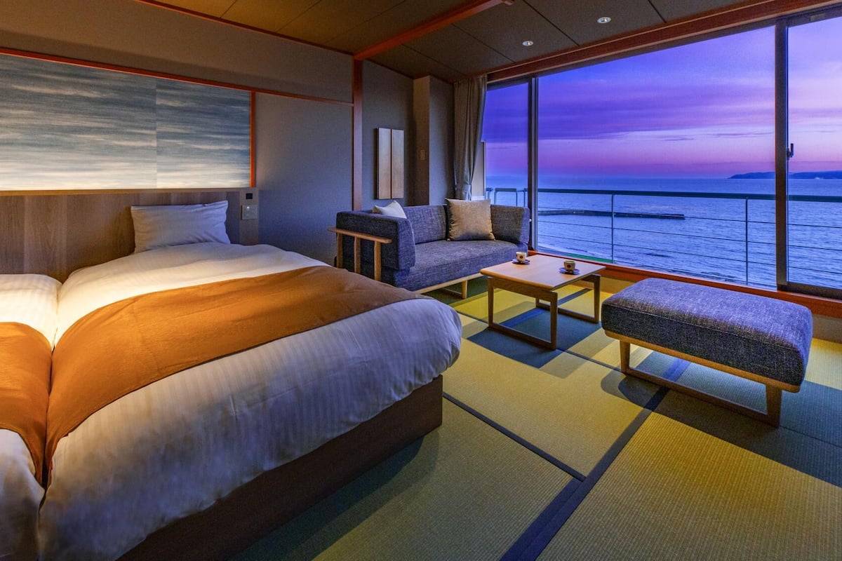 A hotel room with a large bed, a sofa, a small table, and a view of the sea.