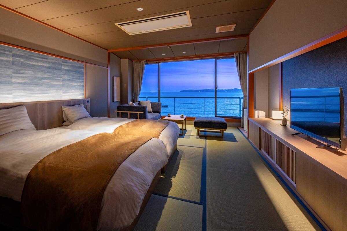 A hotel room with a large bed, a sofa, a small table, and a TV.