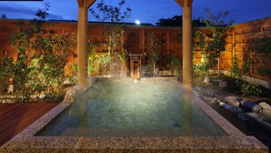 Un área de aguas termales con una pérgola de madera, una piscina de piedra y vegetación circundante.