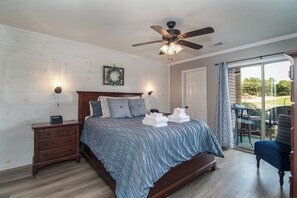 A bedroom with a bed, wooden nightstands, a ceiling fan, and a view of the outdoors through a sliding glass door. - TB 56B Two bedroom Two bathroom True Blue Unit on Golf Course and Pond (Pawleys Island)