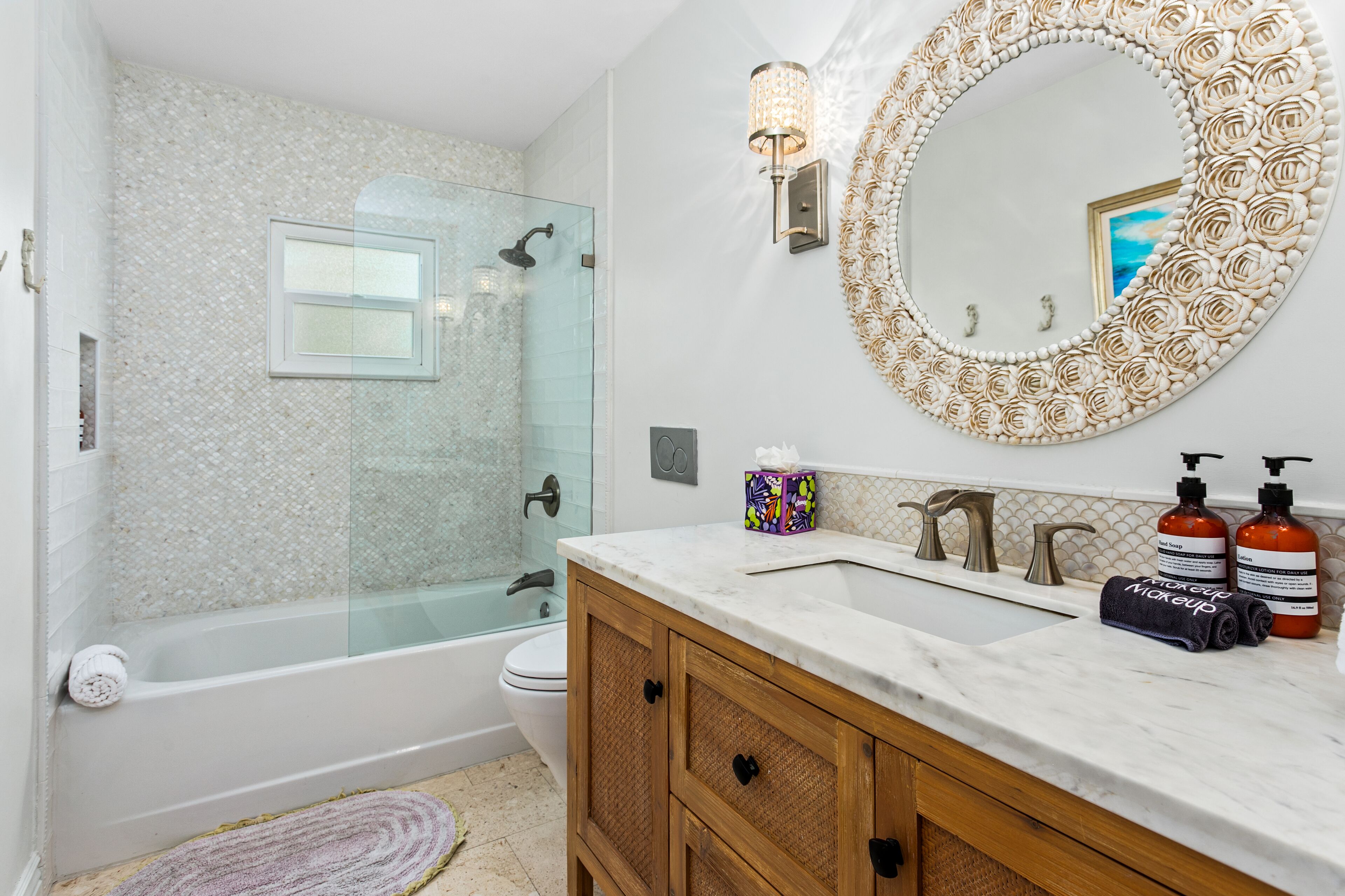 A bathroom with a glass shower enclosure, a white toilet, a marble sink with two soap dispensers, and a wooden vanity.