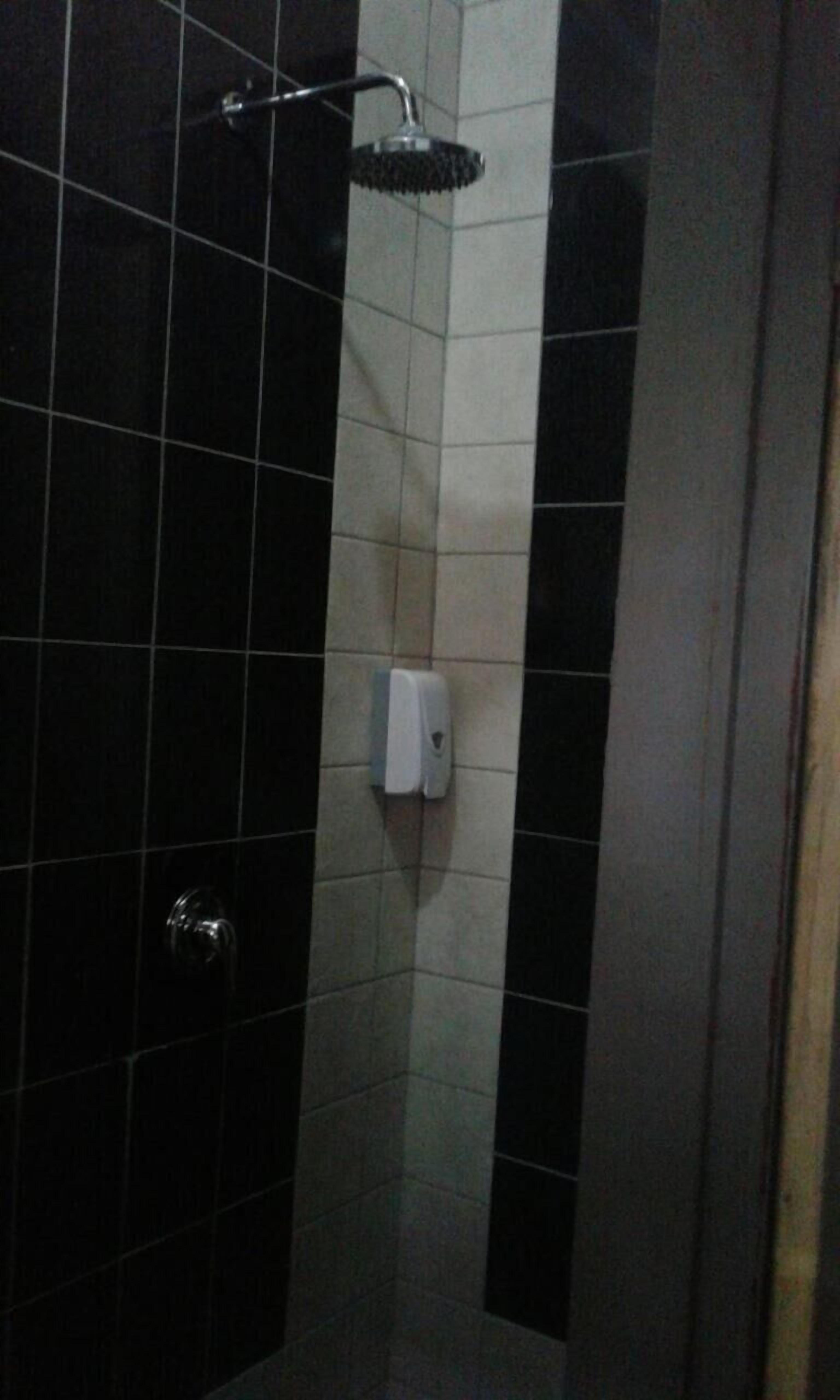 A small, dark-colored shower stall with a handheld showerhead and a soap dispenser on the wall.