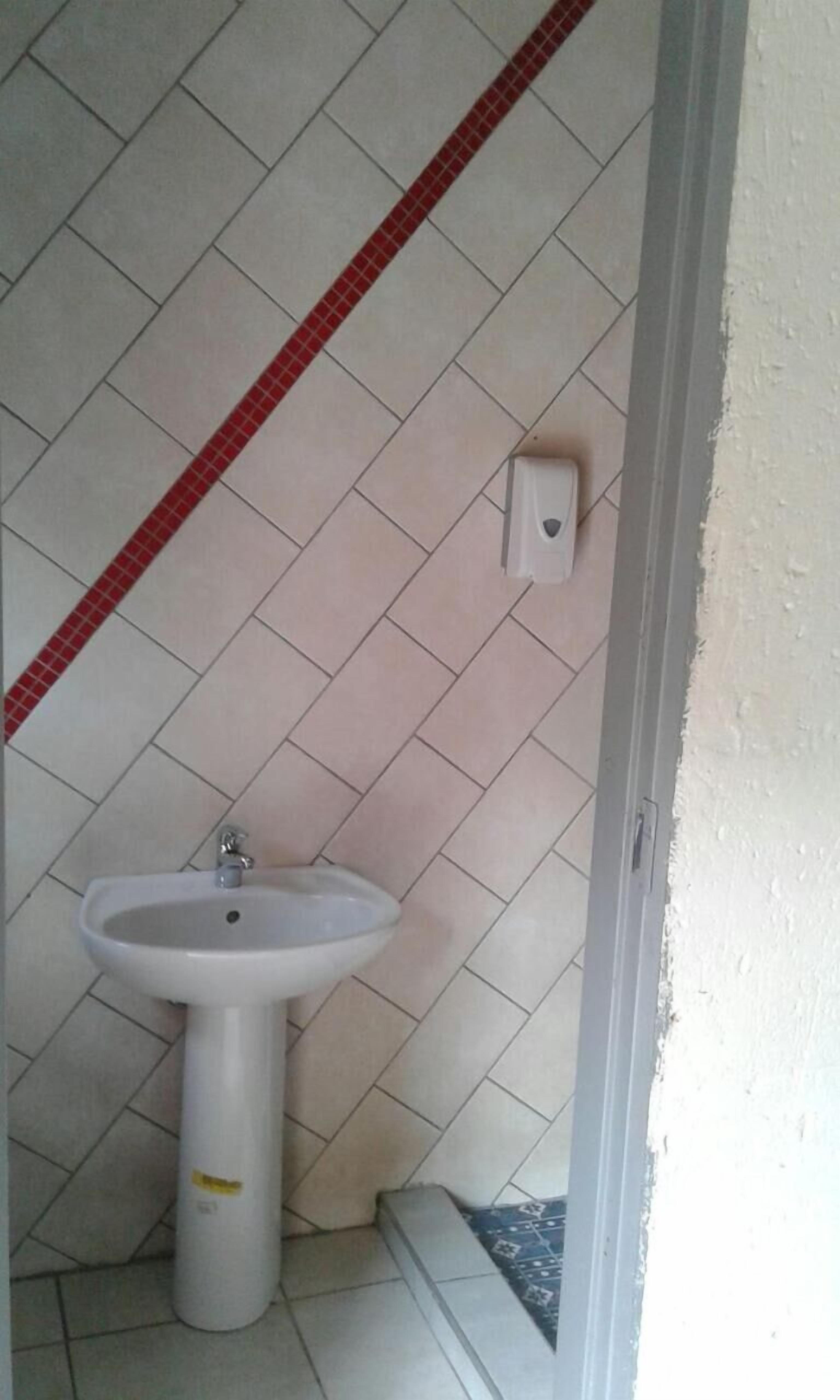 Un baño con un lavamanos blanco pedestal, piso de baldosas rojas y blancas, y una pared blanca con un enchufe eléctrico pequeño.