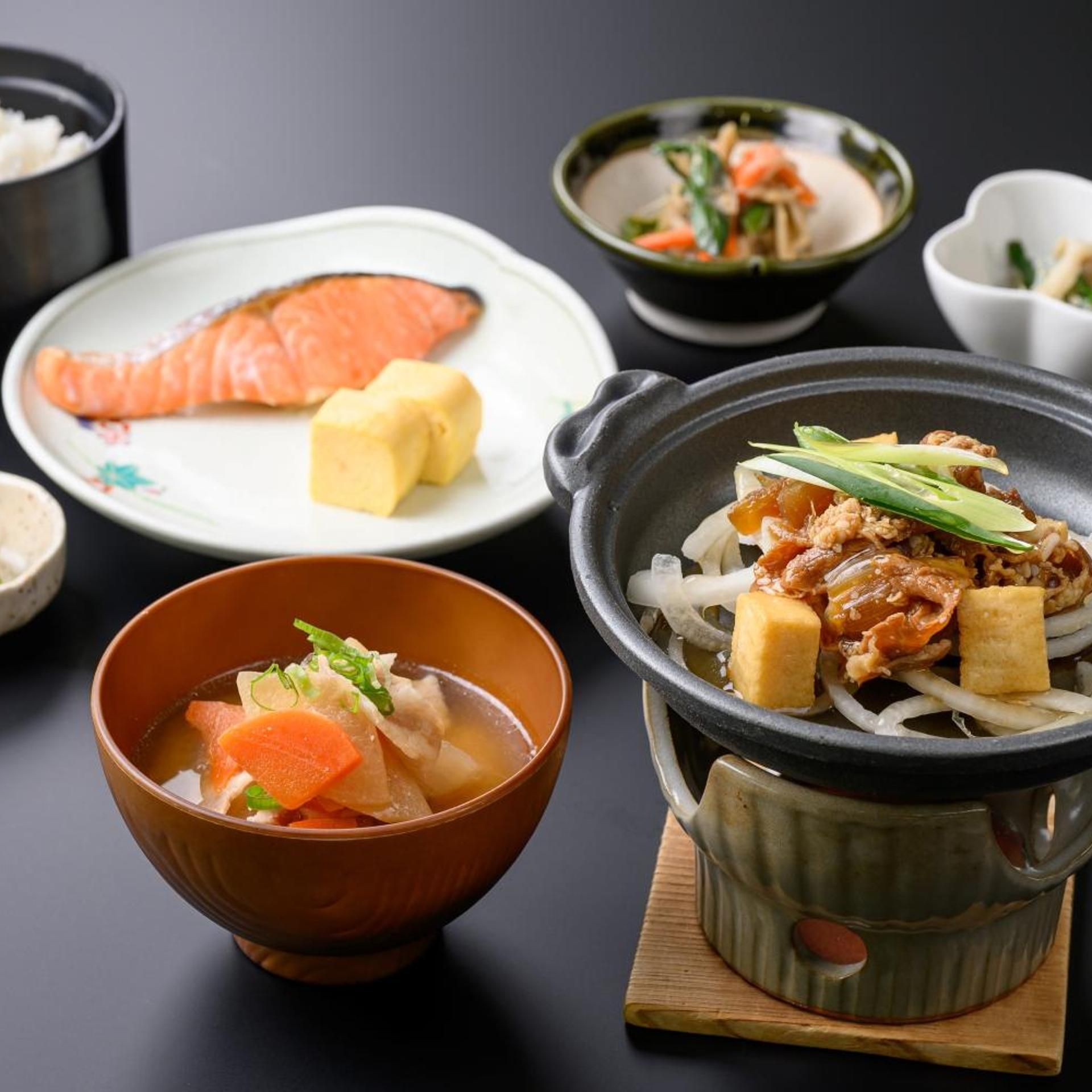 Forskellige japanske retter, heriblandt en skål suppe, en tallerken med laks og tofu, samt en varm gryderet med grøntsager og kød.
