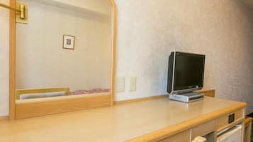 A hotel room with a wooden desk, a television, a mirror, and a small cabinet.