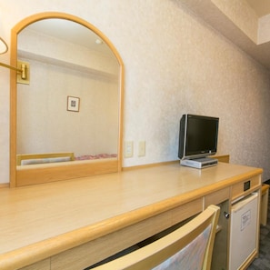 A hotel room with a wooden desk, a television, a mirror, and a small cabinet.