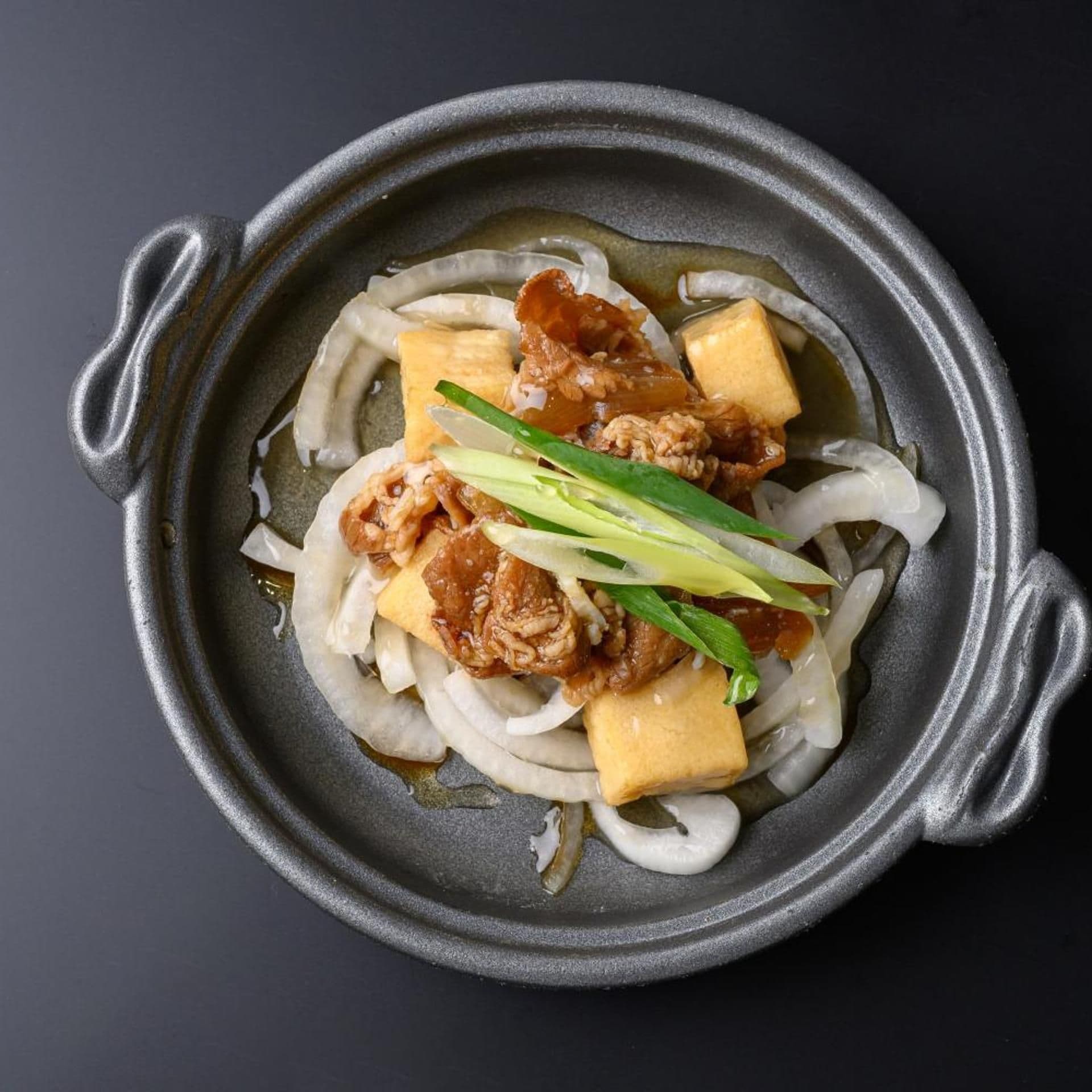 A bowl of food with noodles, tofu, and meat.