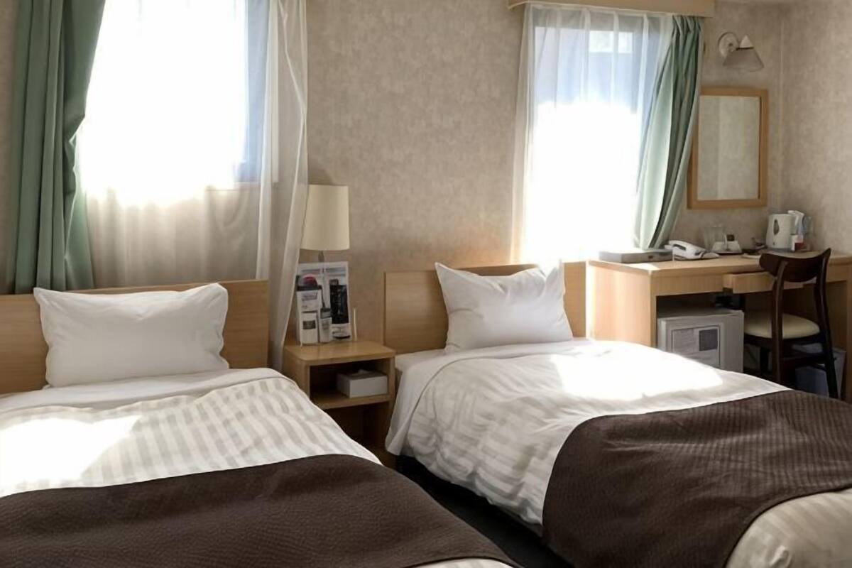 A hotel room with two beds, a desk, a chair, a lamp, a mirror, and a small cabinet.