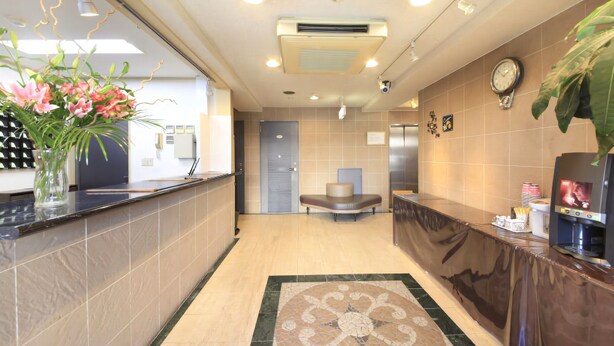 A hotel lobby with a reception desk, a clock, a vending machine, and a decorative rug. - Hachioji Urban Hotel (Hachioji)